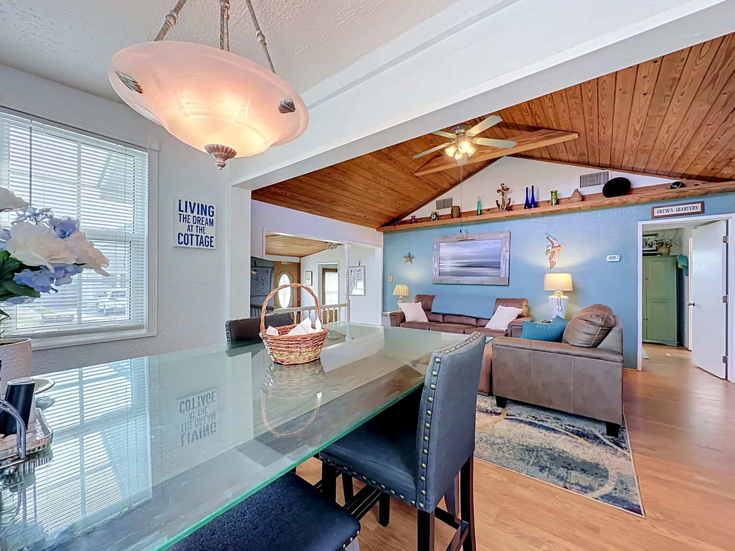 Dining area with a glass-top table looking into an open living room with wood-paneled vaulted ceiling.