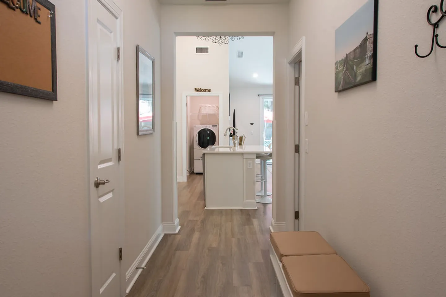 Hallway with wood-look flooring looking into an open kitchen and laundry area.
