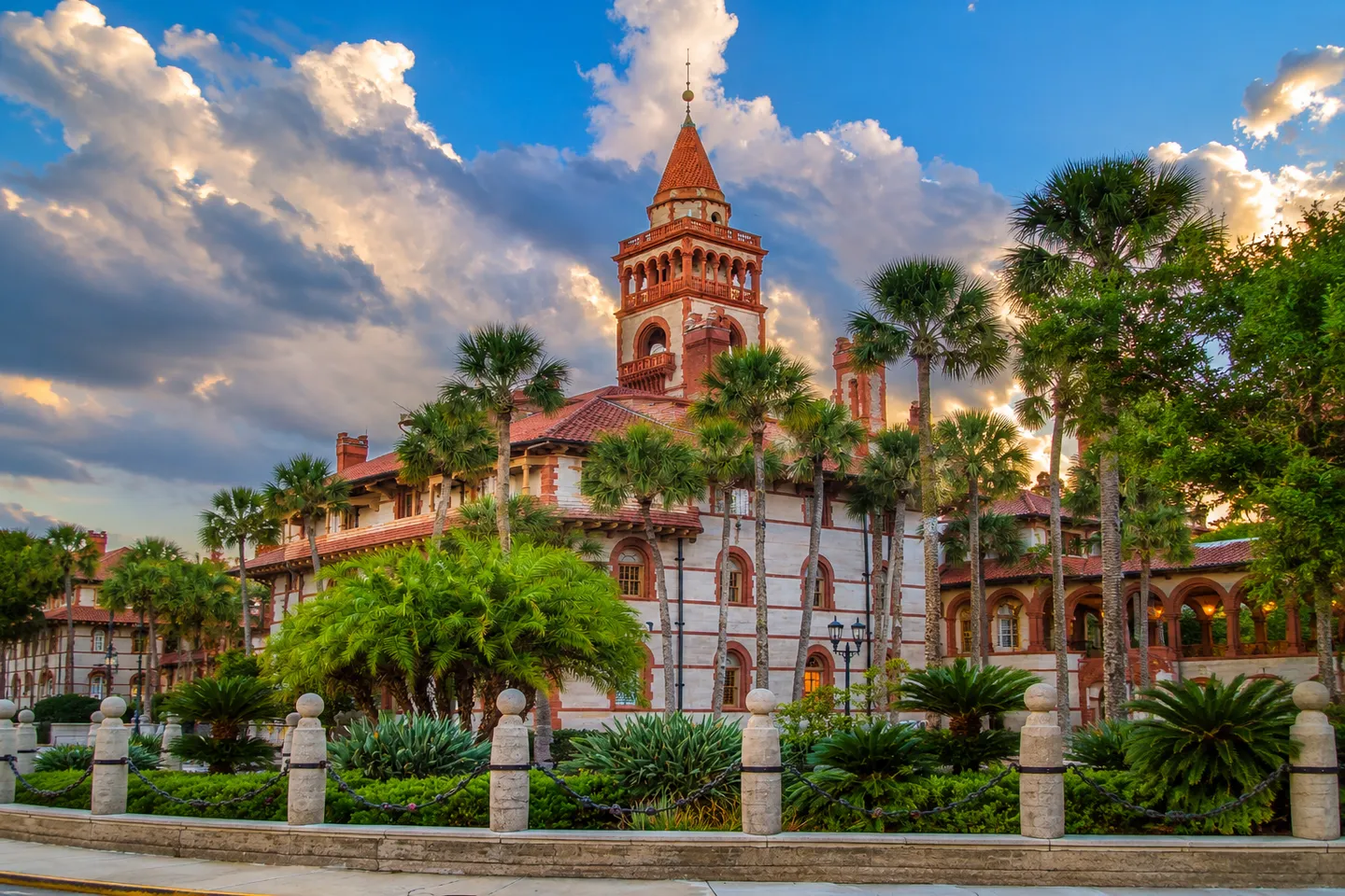 Exterior view of an ornate historic Spanish Renaissance-style building featuring a central tower, red tile roofs, and landscaped grounds with palm trees.