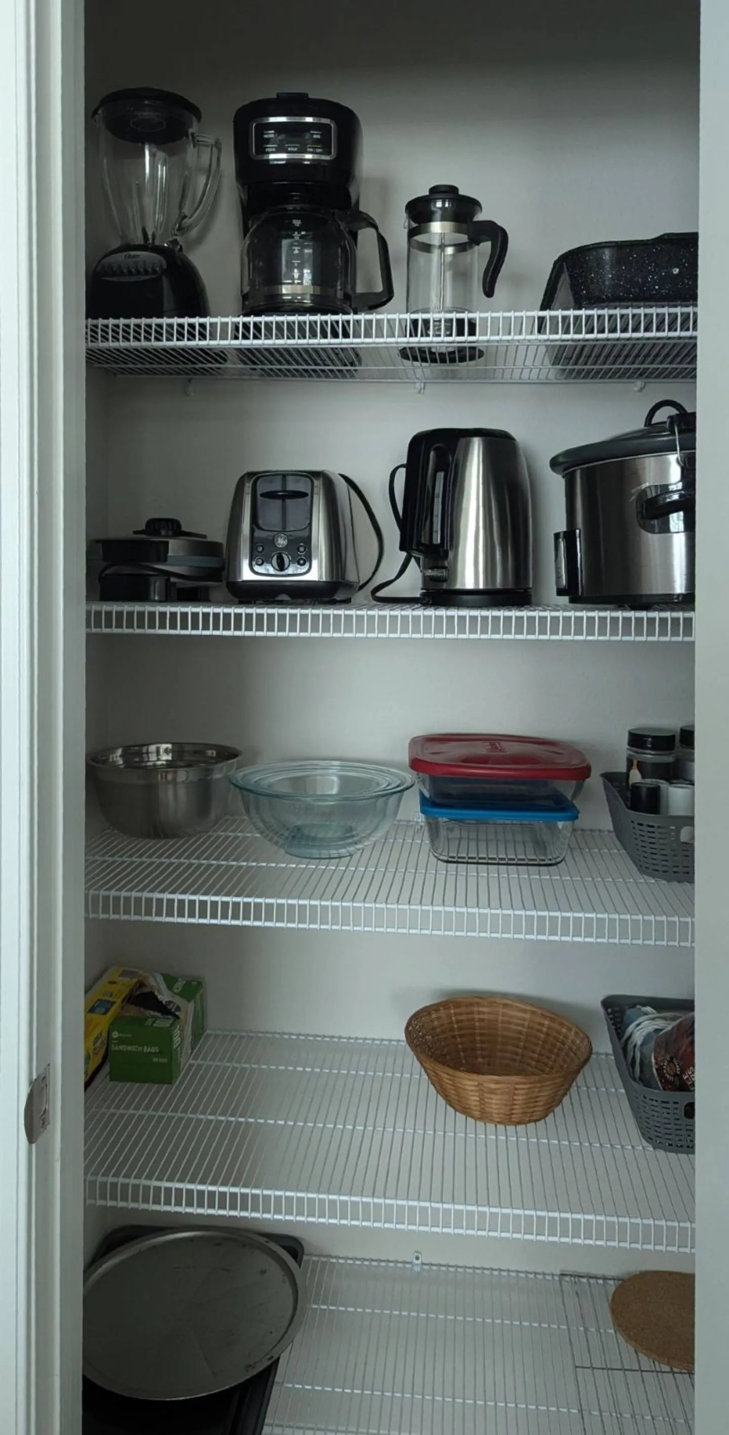Open pantry closet with white wire shelves holding kitchen appliances, mixing bowls, food containers, and baking sheets.