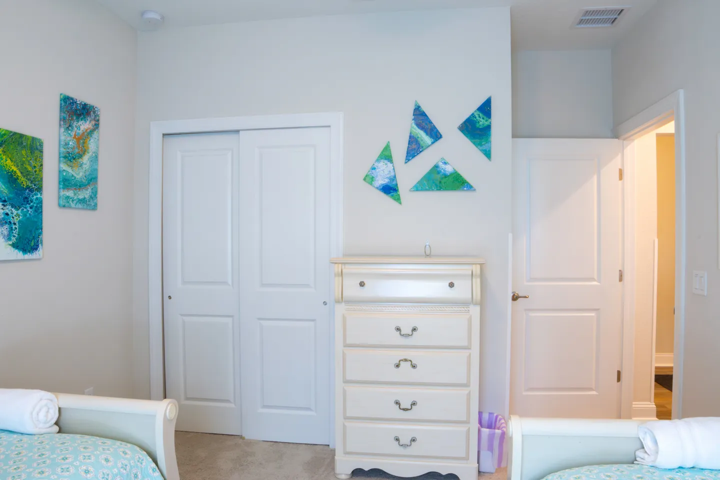 Bedroom corner showing a light wood dresser, closet doors, an open doorway, and footboards of two beds.