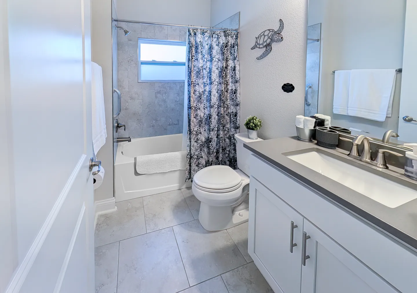 Bathroom with white vanity, toilet, and tiled shower-tub combination featuring a patterned shower curtain.