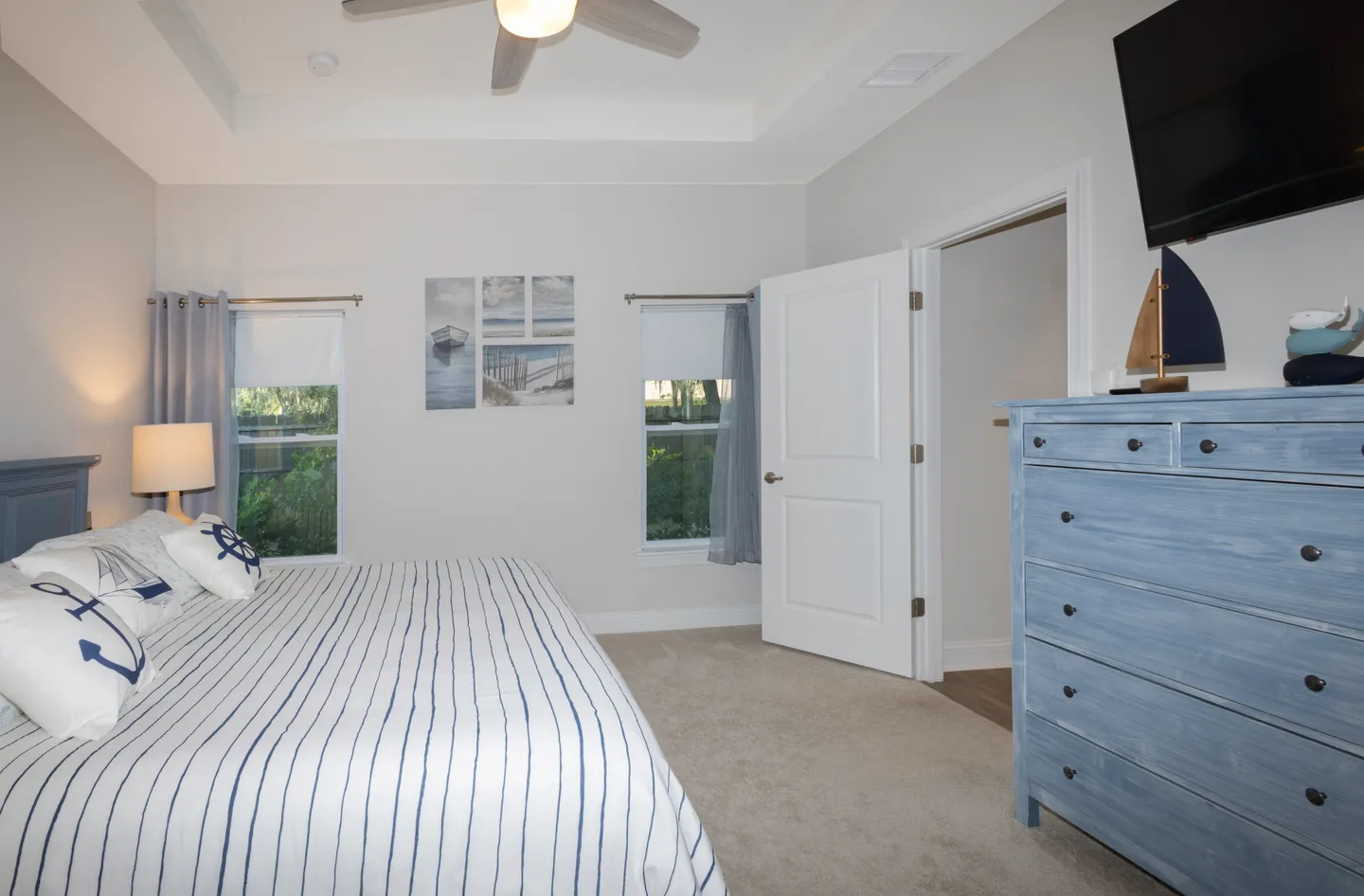 Bedroom with nautical decor, a bed with striped bedding, a light blue wooden dresser, and two windows.