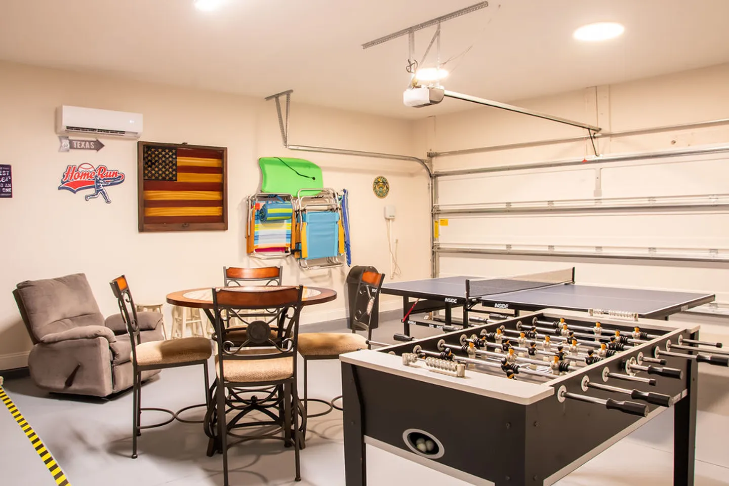 A converted garage game room featuring a foosball table, a ping-pong table, and a round game table with chairs.