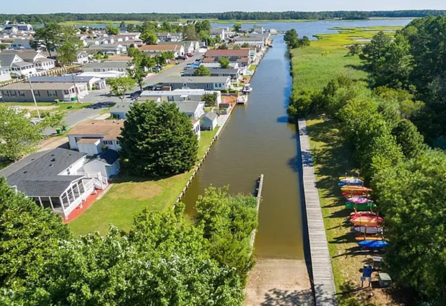 Aerial view of a canal with a boat launch, boardwalk, and stored kayaks next to a residential community.