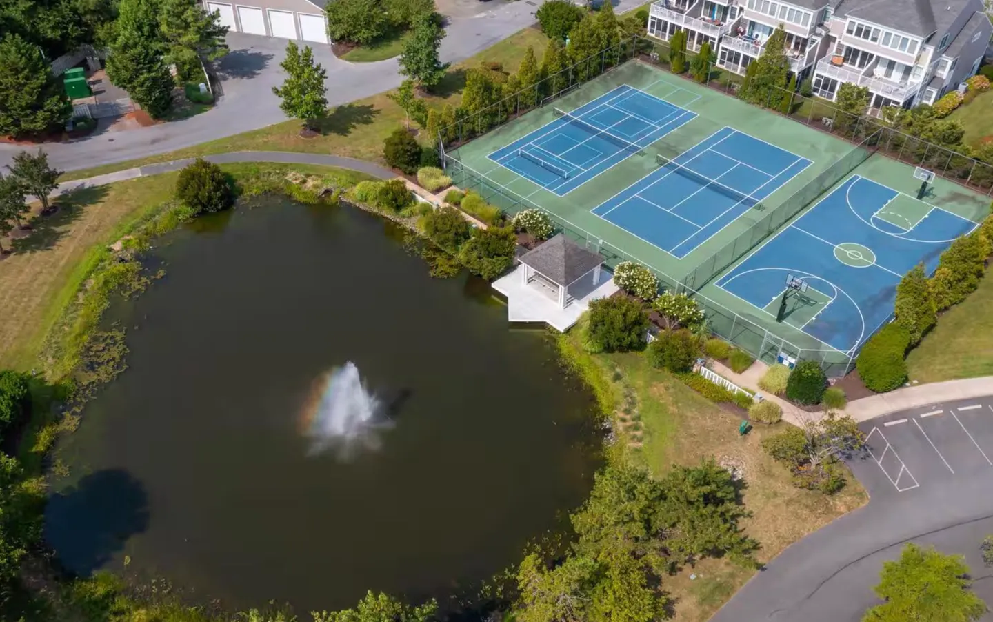 Aerial view of a community pond with a fountain, gazebo, tennis courts, and basketball court.