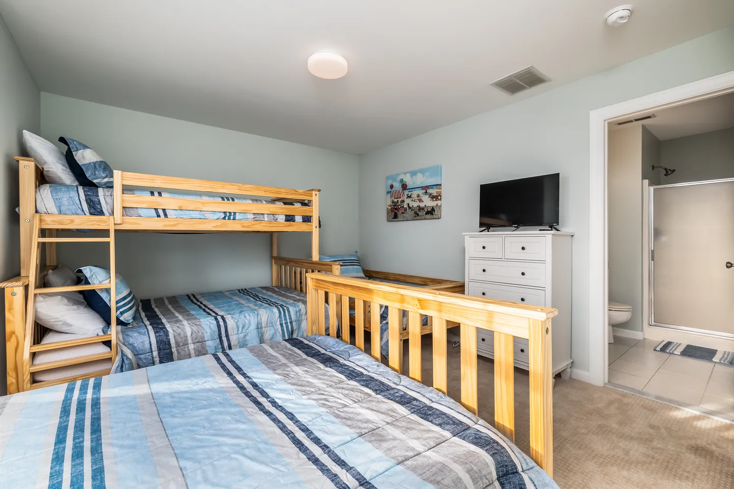 Bedroom with wooden bunk beds, blue striped bedding, a dresser with a TV, and an open doorway to an ensuite bathroom.