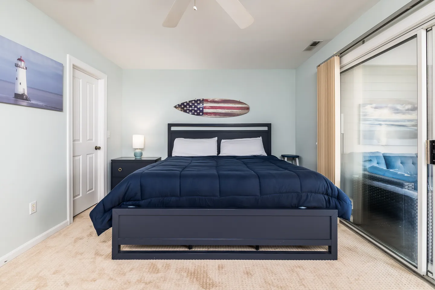 Bedroom with a dark wood bed frame, navy blue comforter, light blue walls, and a sliding glass door.