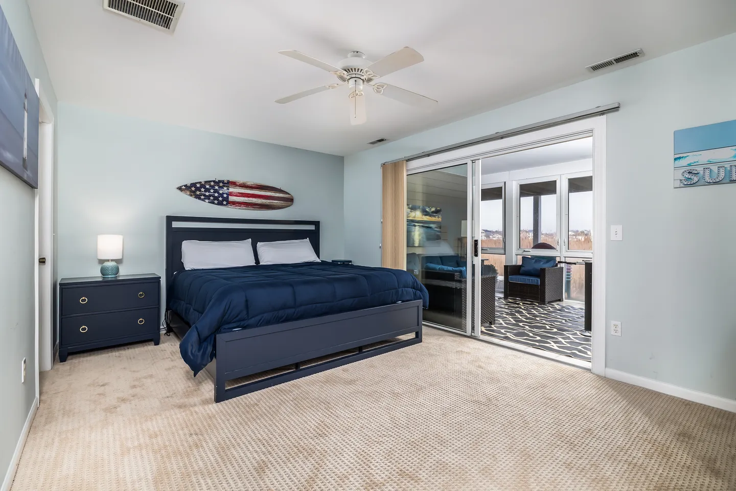 Bedroom with blue bed frame, patterned carpet, and sliding glass doors opening to an enclosed porch.