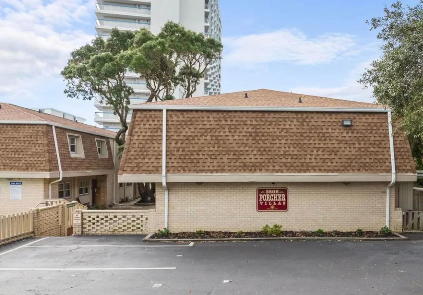 Exterior view of Porcher Villas featuring light brick walls and a mansard roof in front of an asphalt parking lot.
