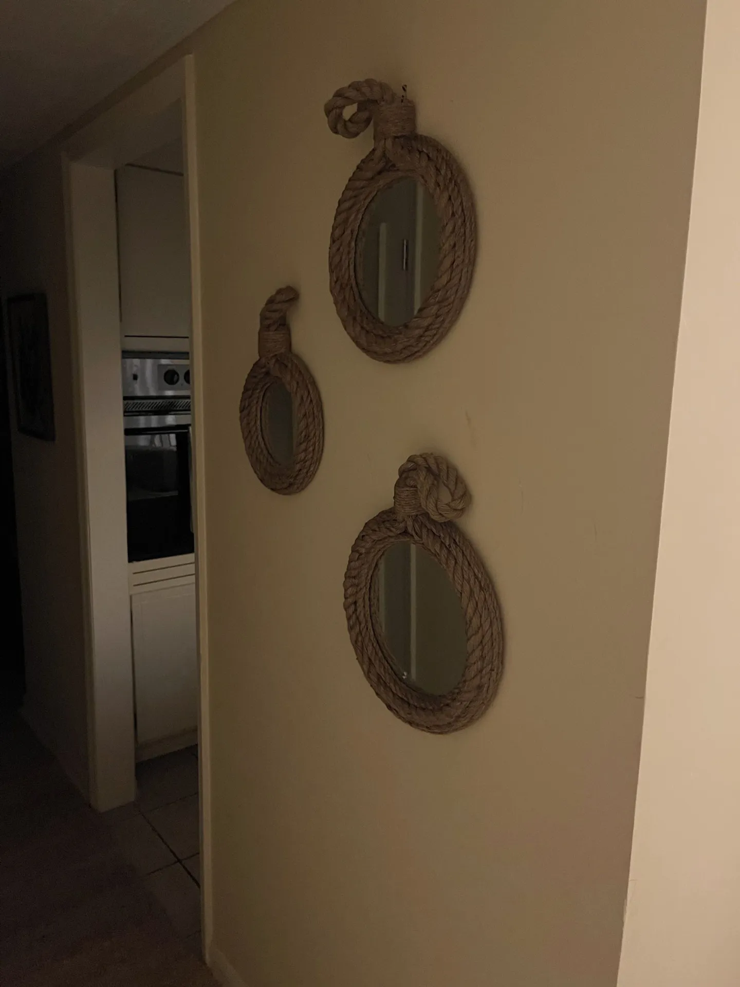 A hallway wall decorated with three round mirrors framed with thick rope hanging near an open doorway.