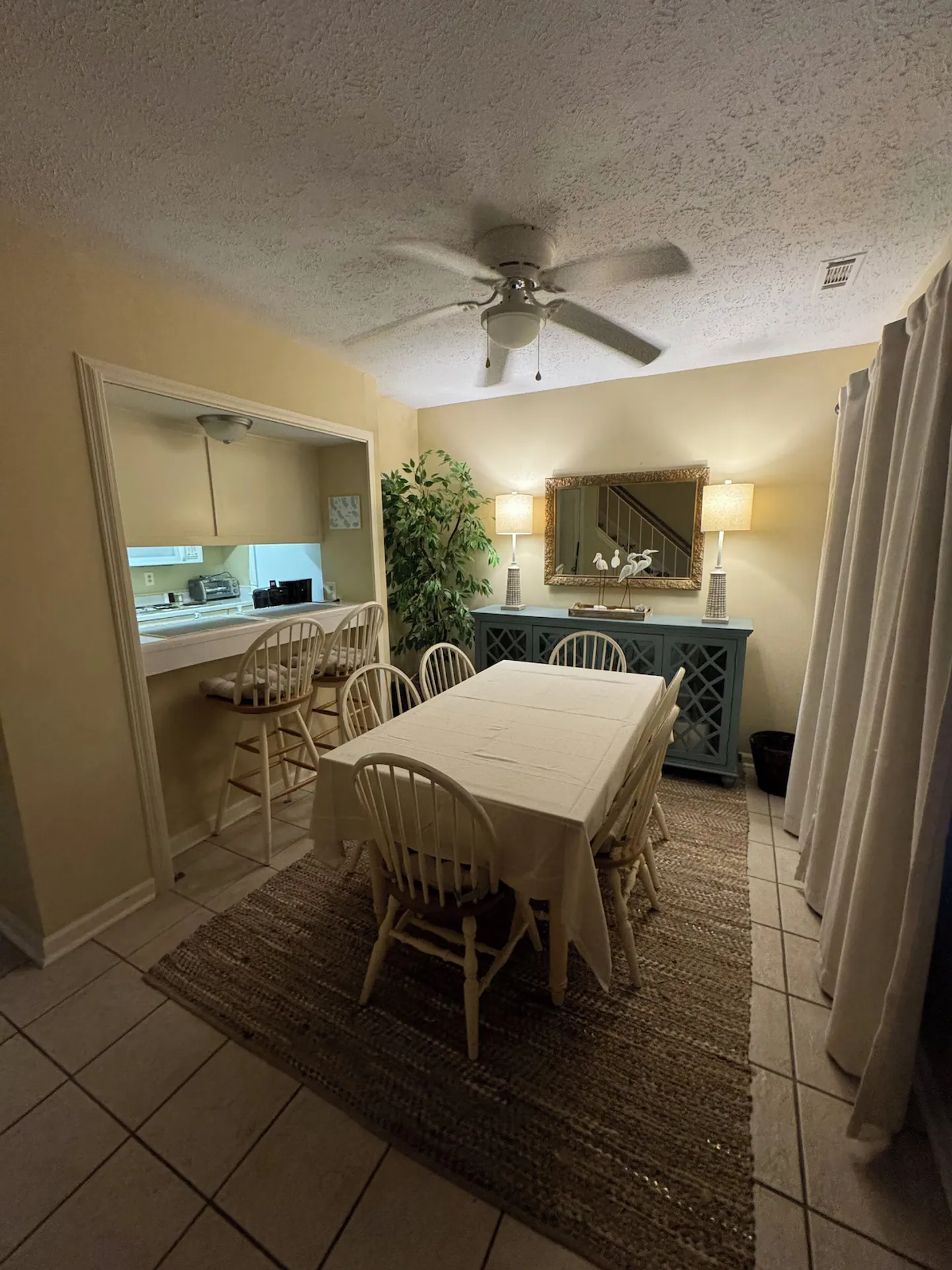 Dining area with a table and chairs over a woven rug, adjacent to a kitchen pass-through counter with barstools.