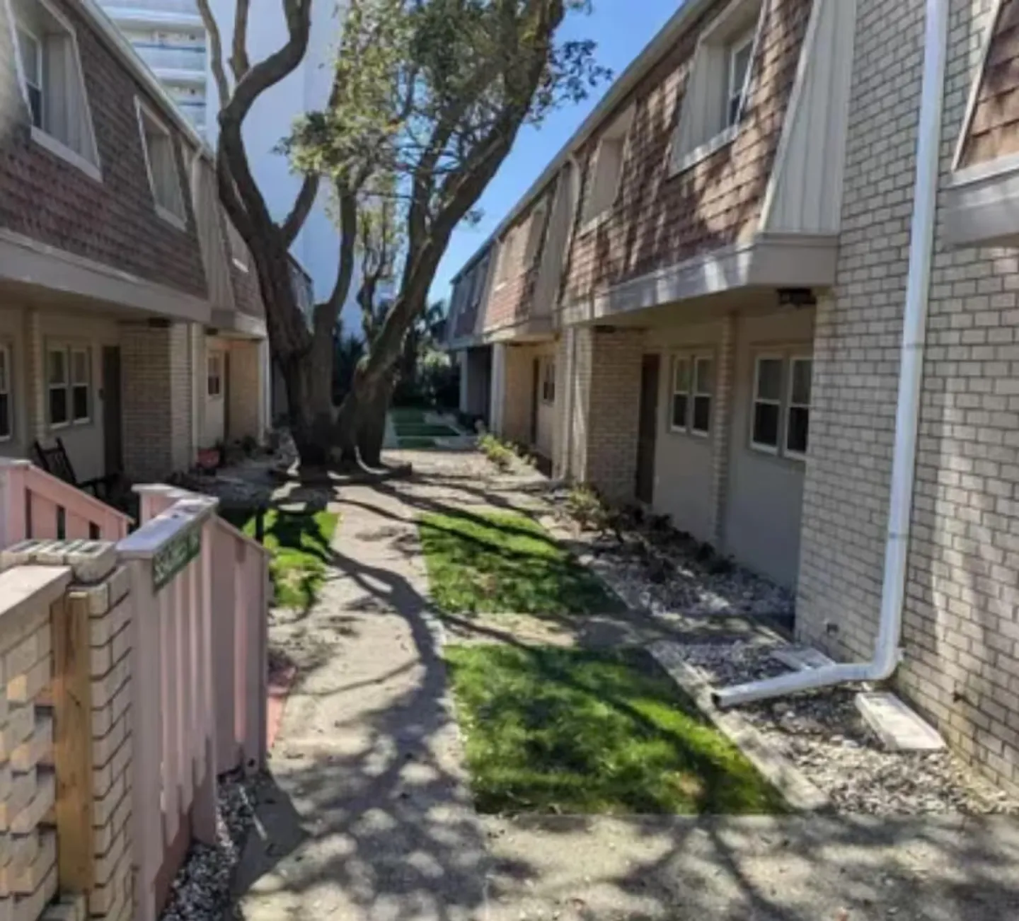Outdoor courtyard walkway situated between two-story townhome buildings with trees casting shadows.