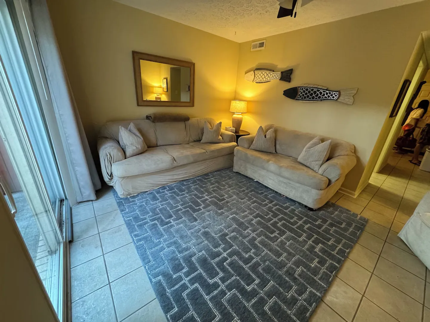 Living room featuring a beige sofa, loveseat, patterned blue rug, tiled flooring, and sliding glass doors.