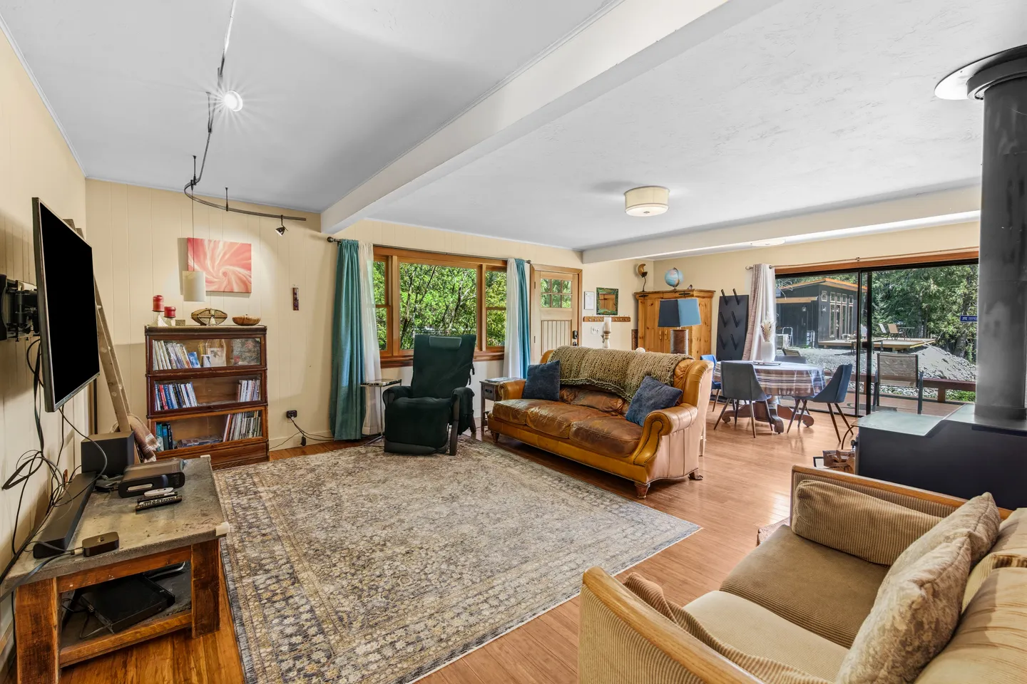 Living room with leather sofa, recliner, large area rug, television, wood-burning stove, and a dining area in the background.