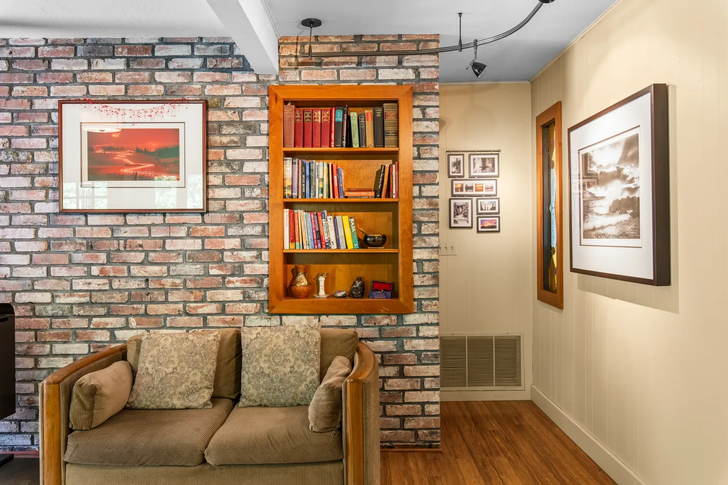 Living area featuring an exposed brick wall with a built-in wooden bookcase, an armchair, and framed artwork on the adjacent paneled wall.