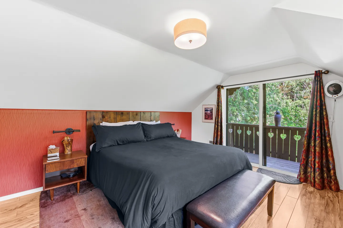 Bedroom with a bed dressed in dark linens, a wooden headboard, an orange accent wall, and sliding glass doors leading to a balcony.