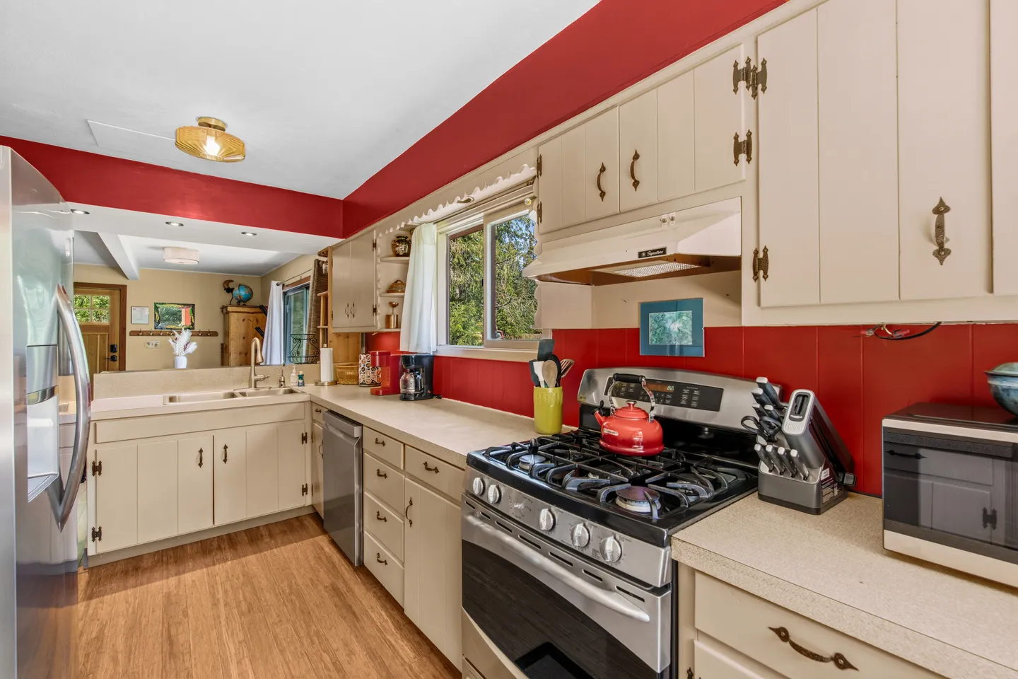 Kitchen with off-white cabinetry, red accent walls, stainless steel appliances, and a window above the counter.