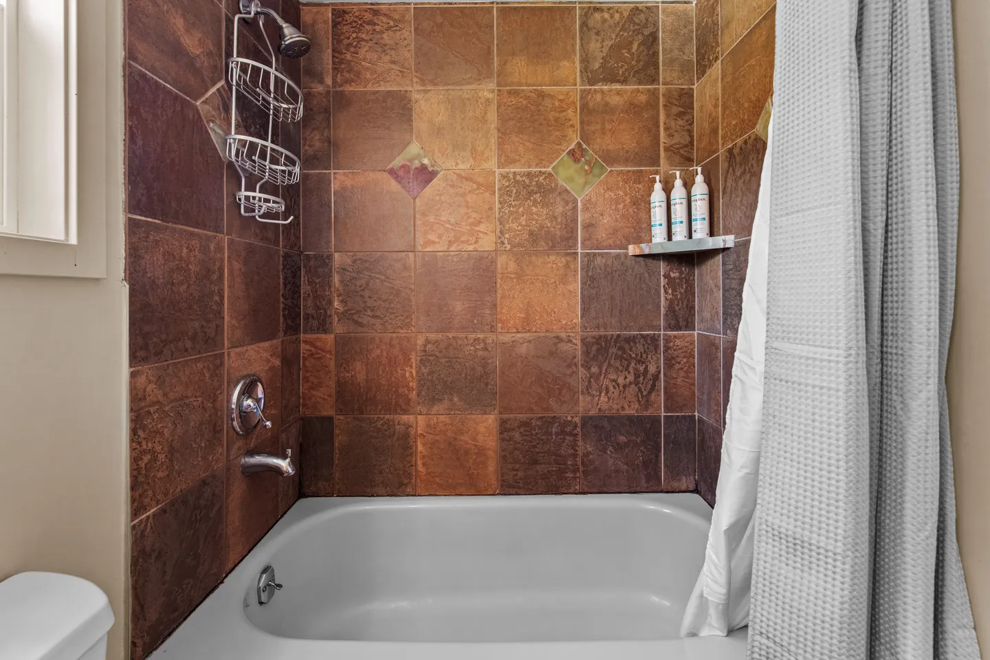 Bathroom bathtub and shower combination featuring earth-toned tile surround and a white textured shower curtain.