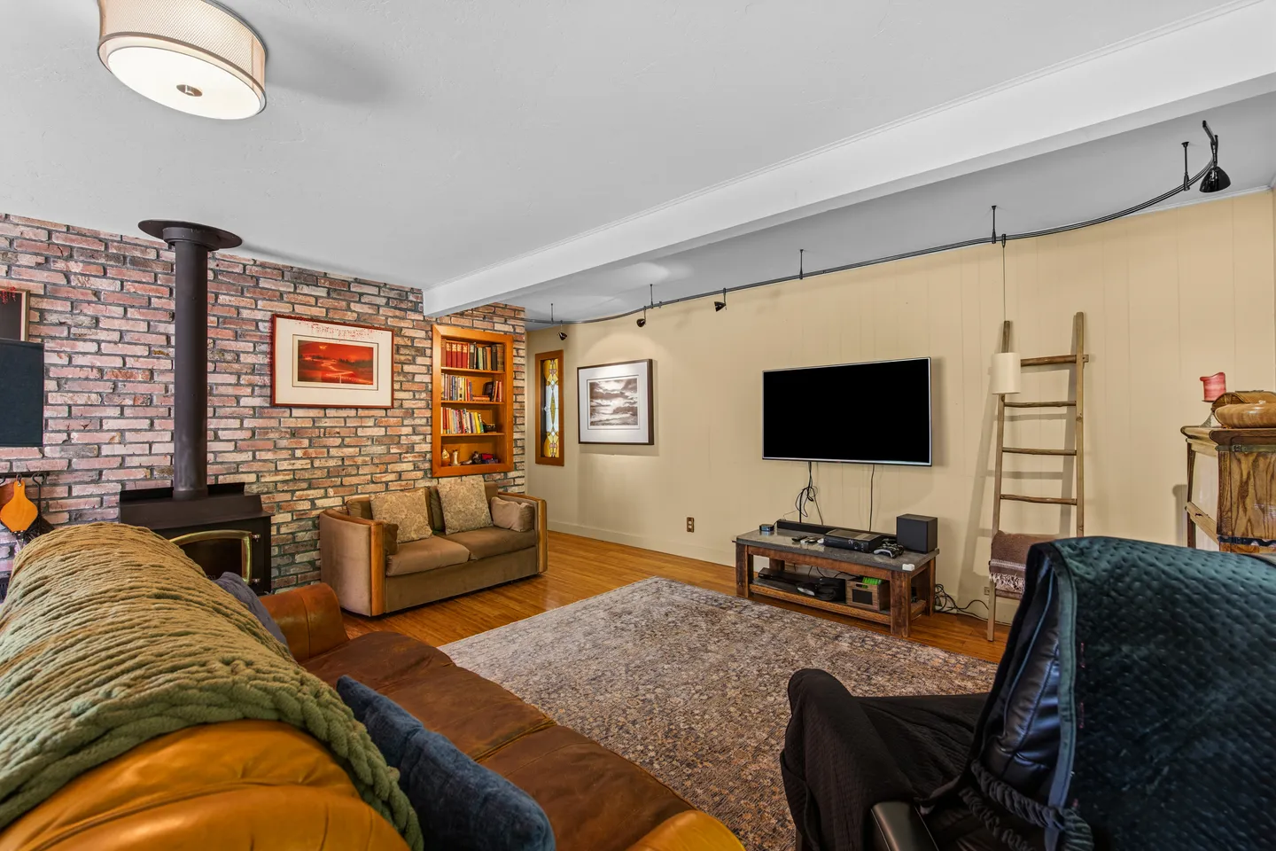 Living room with brick accent wall, wood-burning stove, wall-mounted TV, and sofa seating around an area rug.