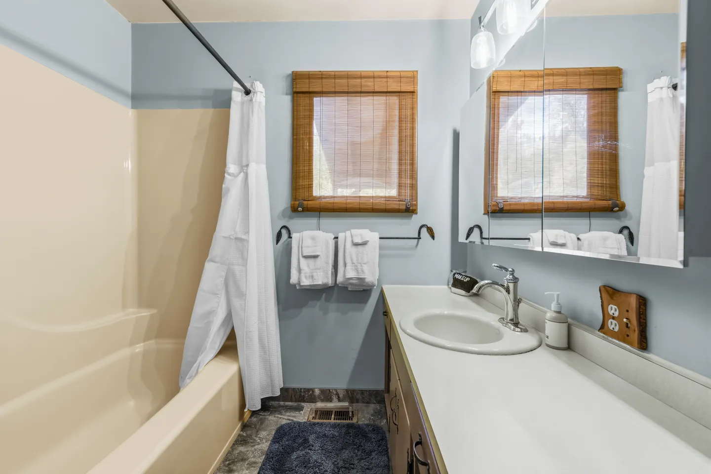 Bathroom with a bathtub and shower combination, vanity counter with sink, and a window with a woven wood shade.