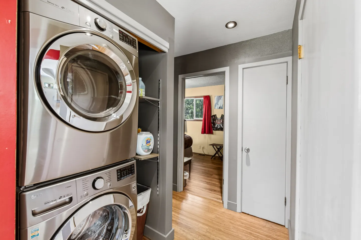 Stacked stainless steel washer and dryer in a hallway alcove next to interior doorways.