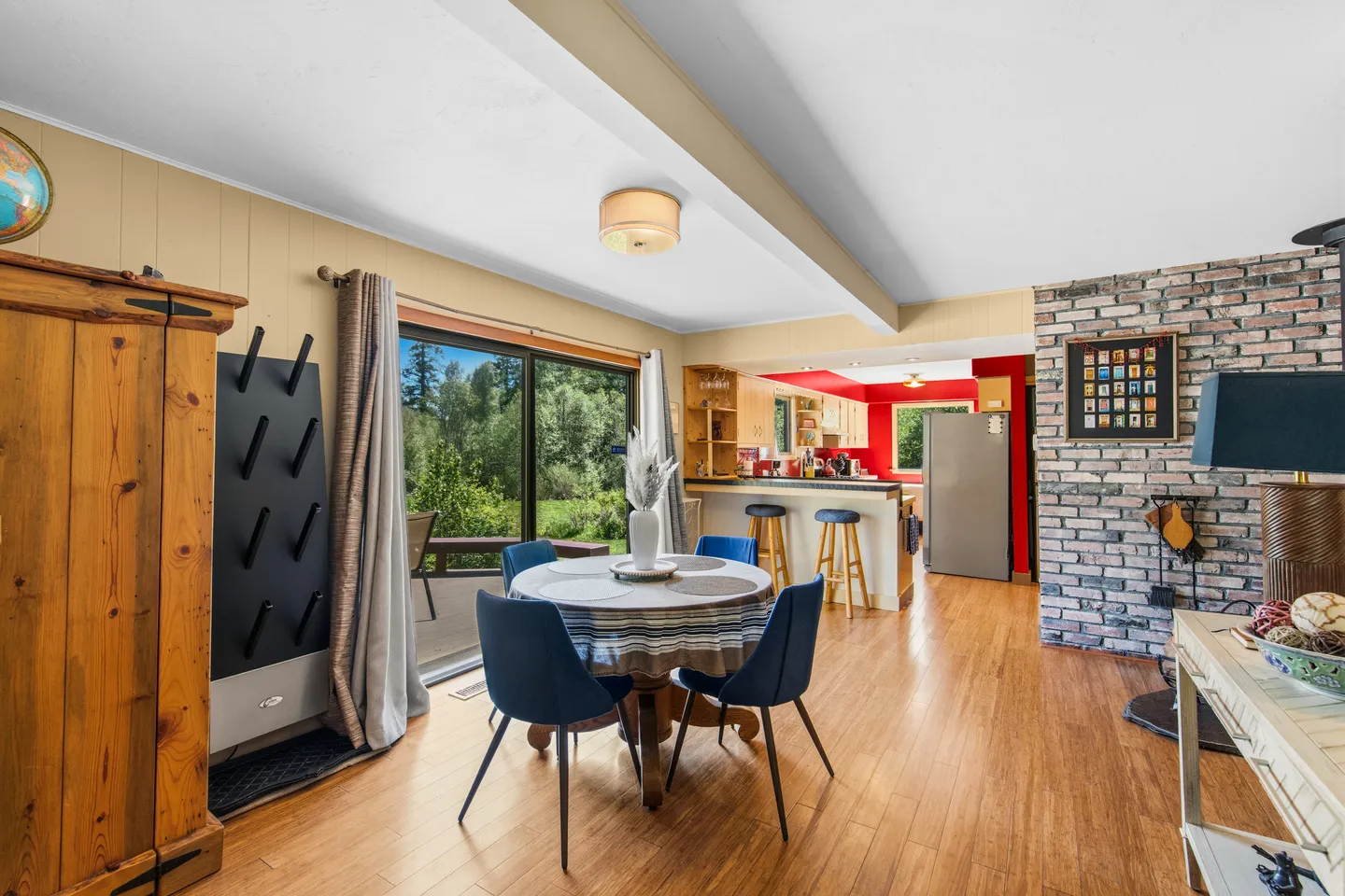 Dining area with a round table and blue chairs adjacent to a kitchen and sliding glass doors leading outside.