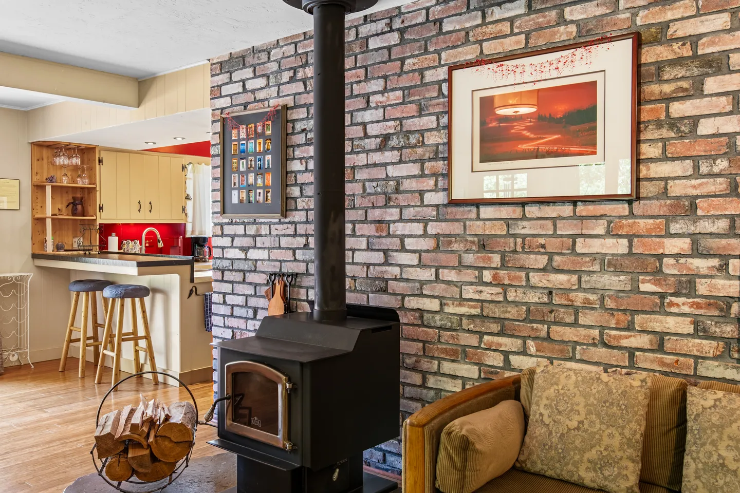A black wood-burning stove set against an exposed brick wall next to a sofa and with a view of the adjacent kitchen.