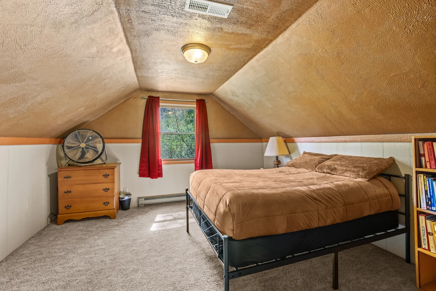 Bedroom with sloped textured ceilings, a bed with brown bedding, a dresser, and a window with red curtains.