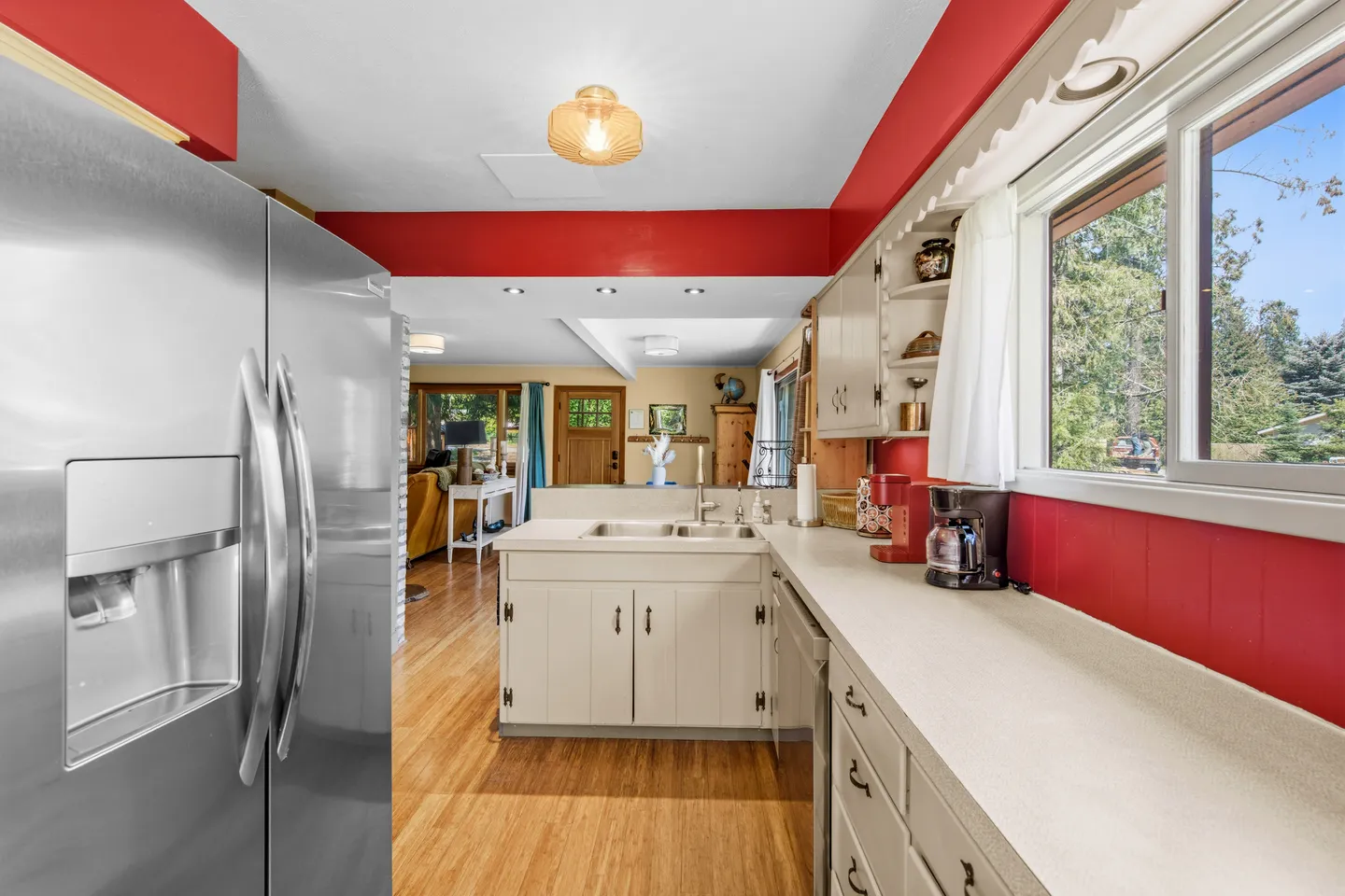 A kitchen with bold red walls, light-colored countertops and cabinetry, a stainless steel refrigerator, and a view into the living room.