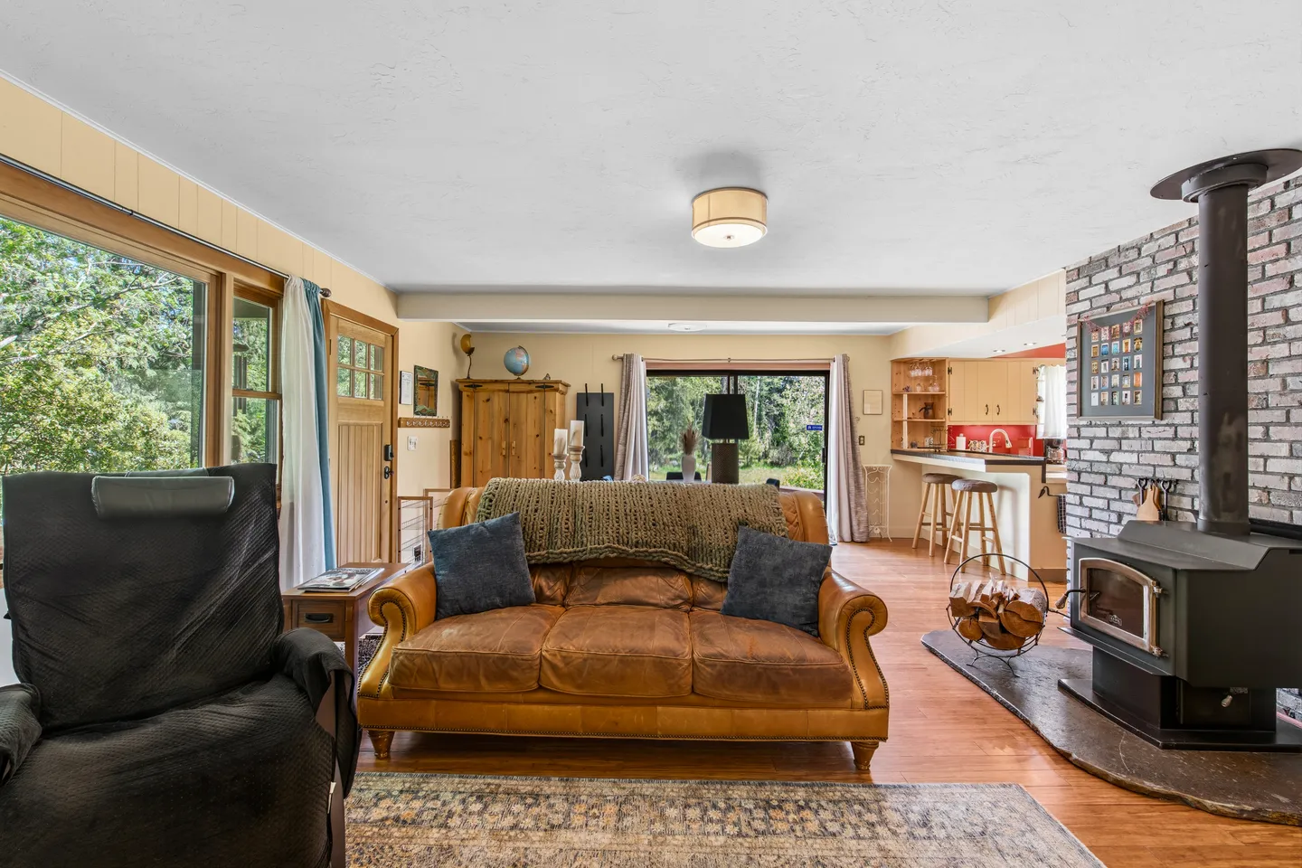Open-concept living room with a brown leather sofa, wood-burning stove, and a view into the kitchen and dining area.