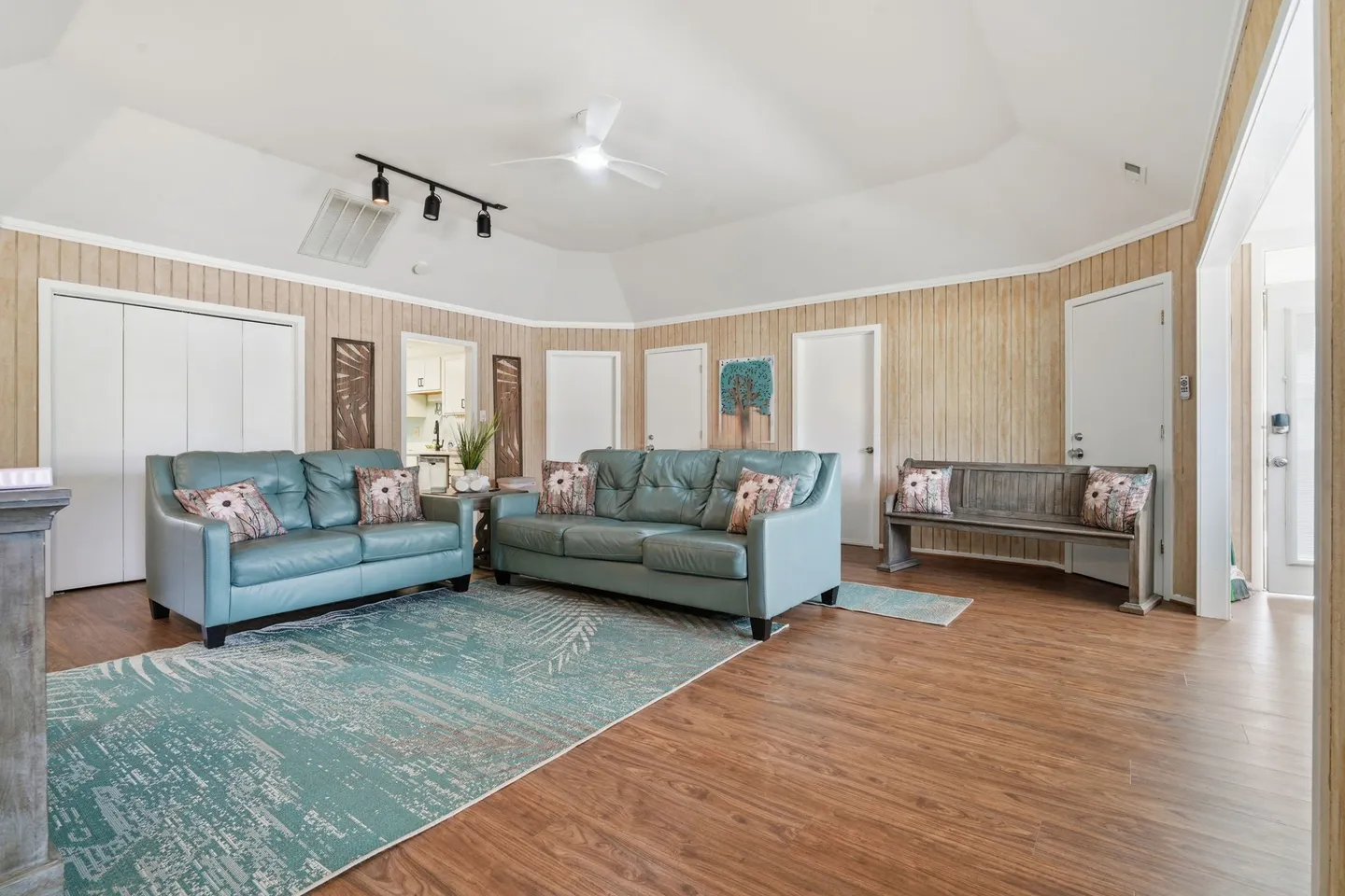 Living room with light blue leather sofas, a patterned teal area rug, wood-look flooring, and paneling on the walls.