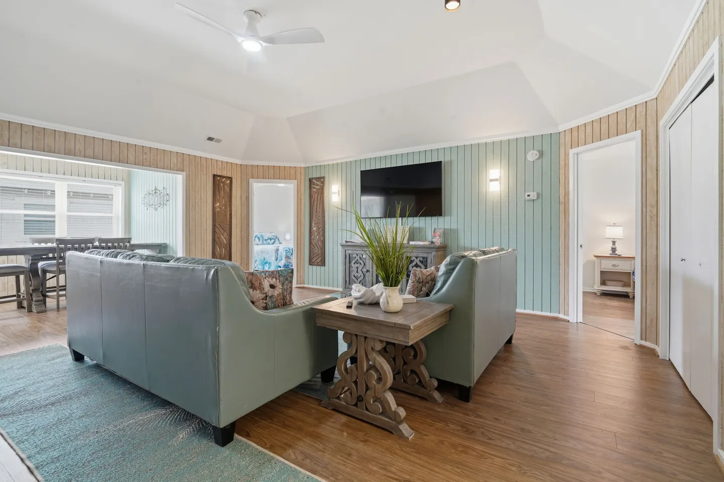 Living room featuring vaulted ceiling, wood-look flooring, light teal armchairs, a side table, and a wall-mounted TV.