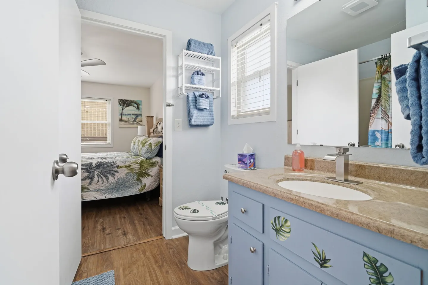 Bathroom with a blue vanity and toilet, showing an open doorway into an adjoining bedroom.