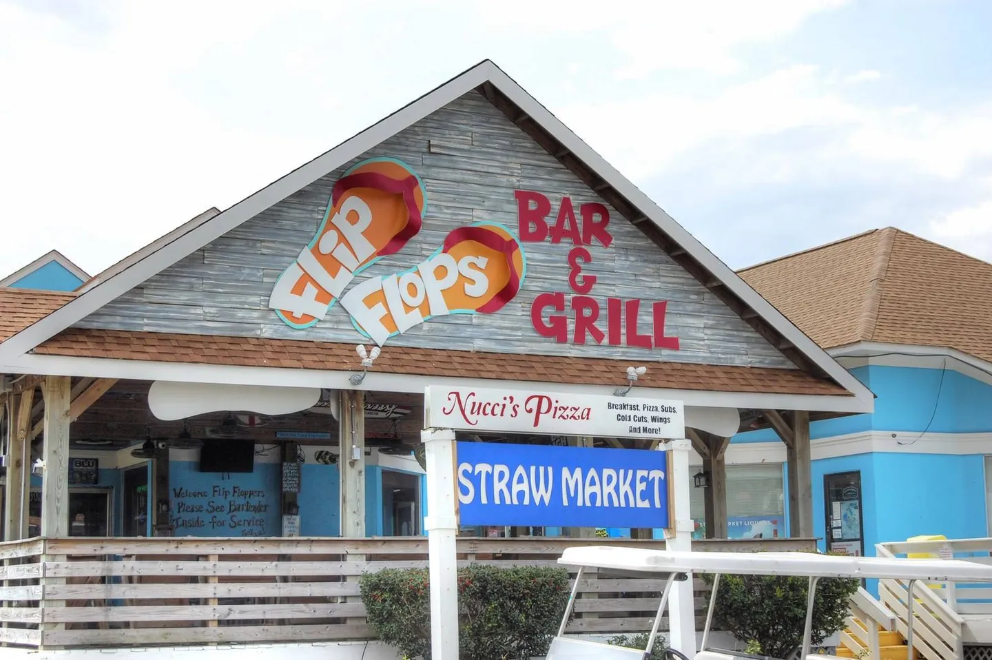 Exterior view of Flip Flops Bar & Grill with a Straw Market sign and golf cart in front.