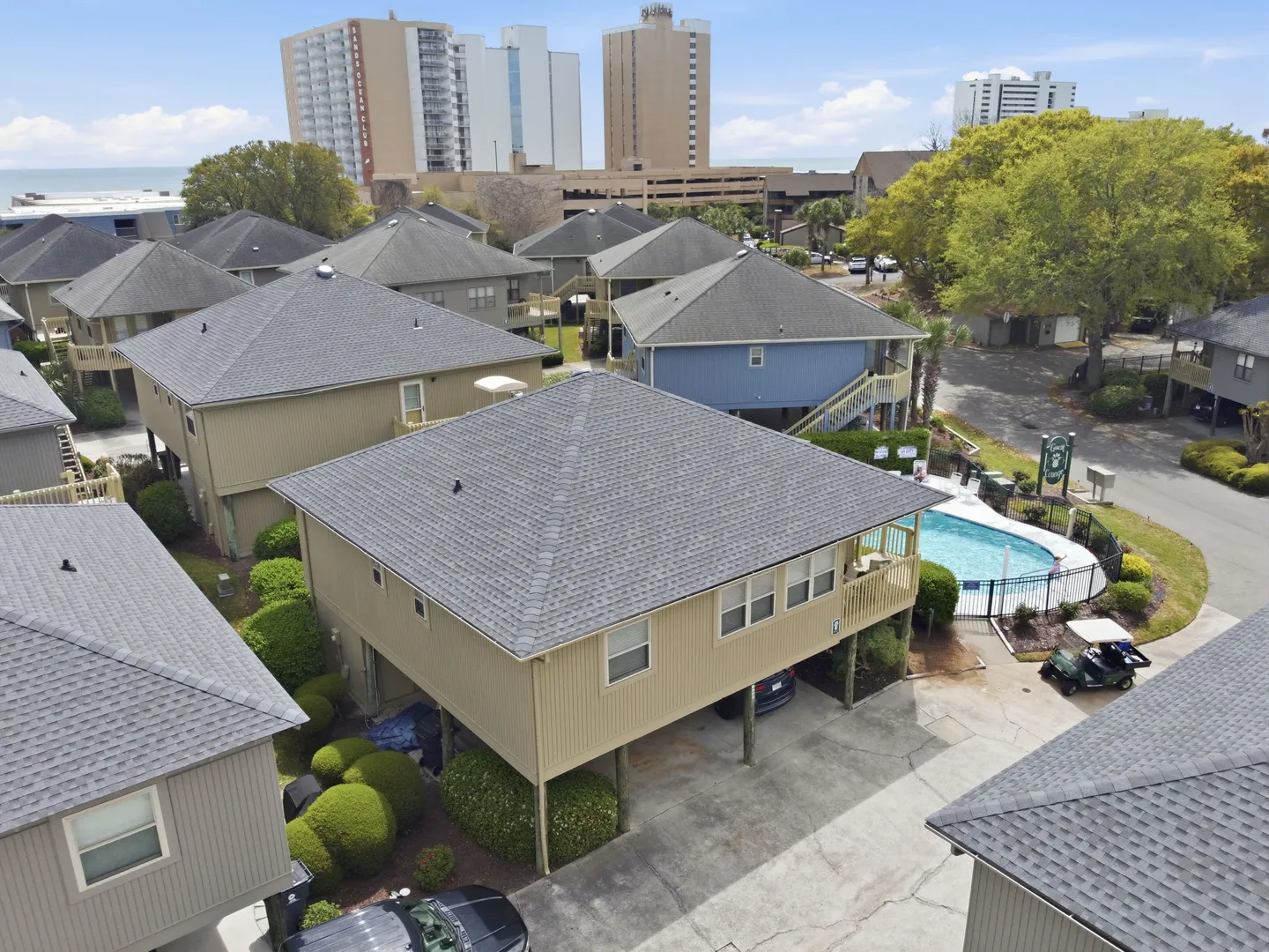 Aerial view of a coastal neighborhood with stilt houses, parking underneath, and a community swimming pool.