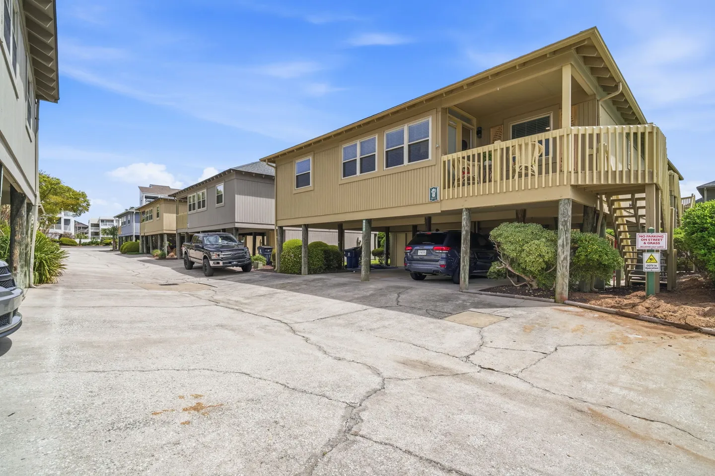 Exterior of elevated vacation homes on pilings along a paved driveway with cars parked underneath.