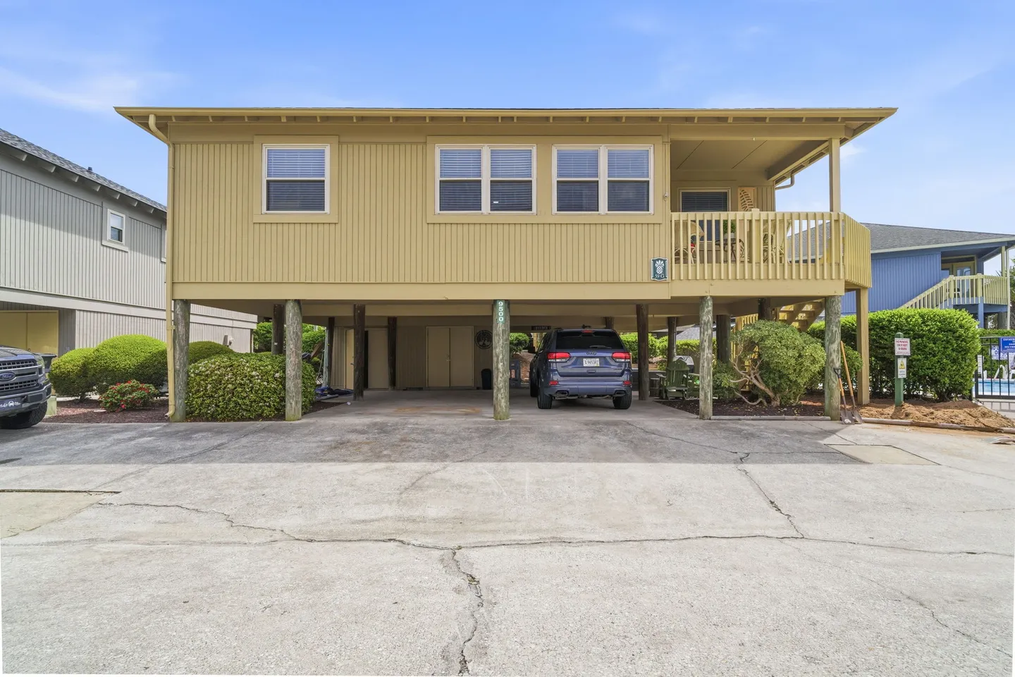 Exterior view of an elevated yellow stilt beach house with covered ground-level parking and a front porch.