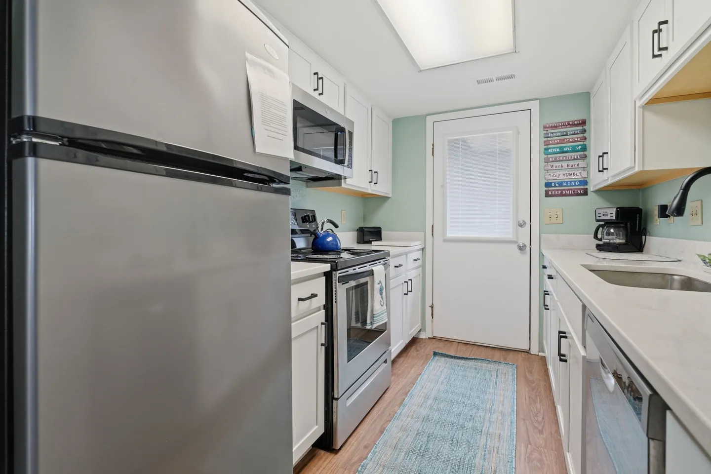 Galley-style kitchen with white cabinetry, stainless steel appliances, and a back door.