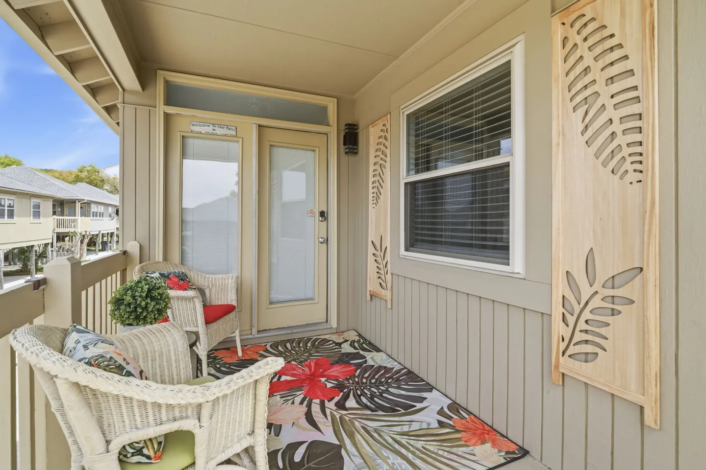 Covered porch with white wicker chairs, a tropical rug, and decorative leaf wall panels near the front entrance.