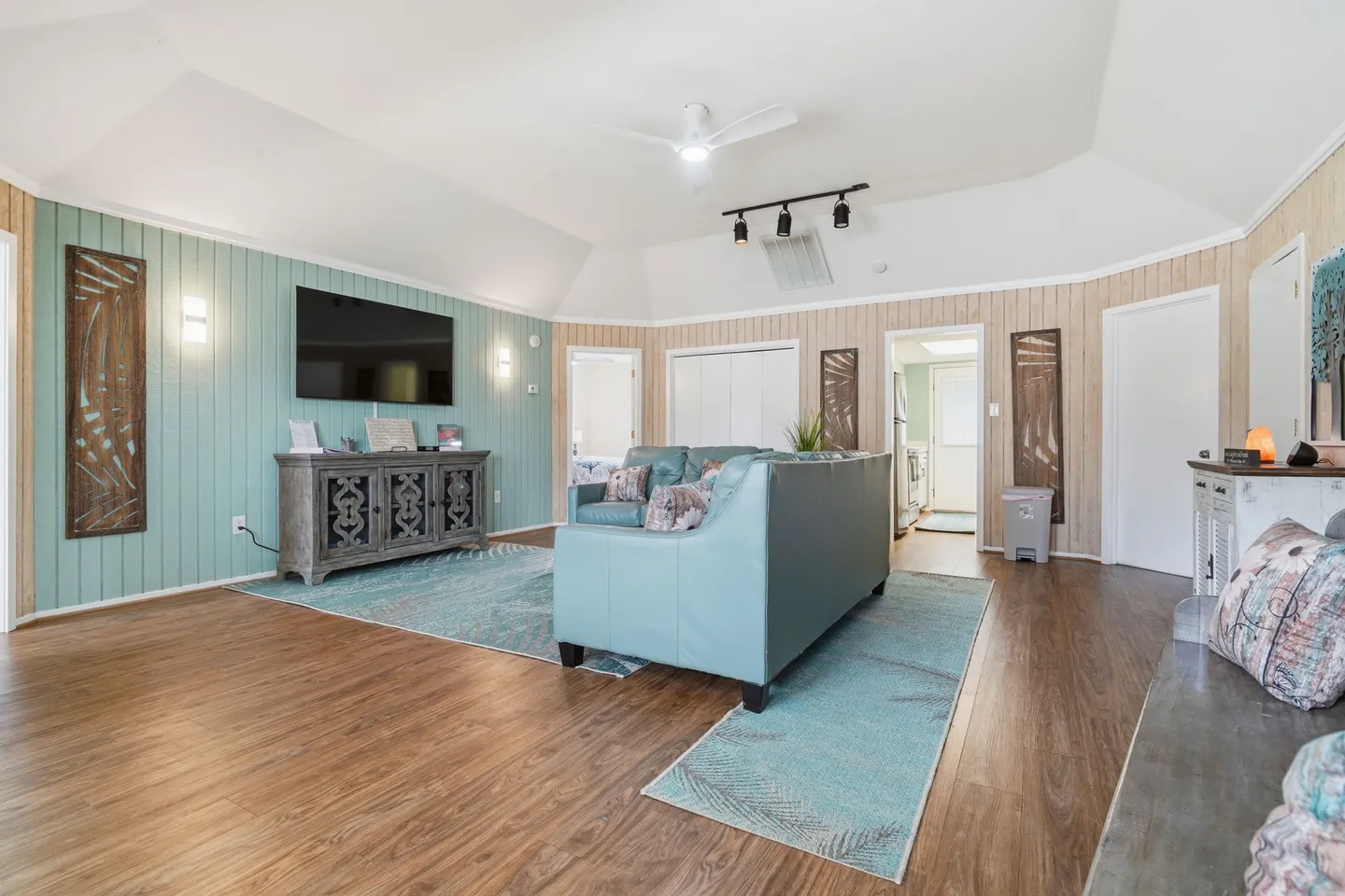 Living room with wood-style flooring, a light blue sofa, vaulted ceiling, and a wall-mounted television over a console cabinet.