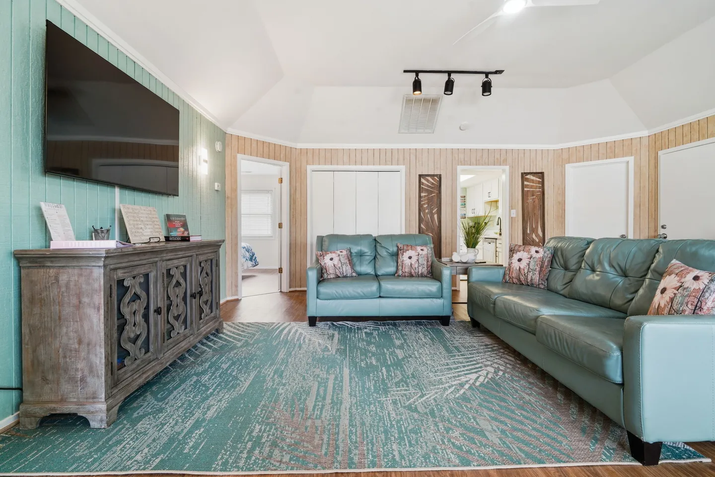 Living room with teal leather sofas, an area rug, a credenza with a wall-mounted TV, and vertical wood-paneled walls.