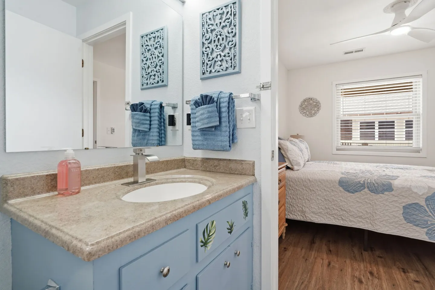 Bathroom vanity with a light blue cabinet and mirror, looking into an adjacent bedroom.