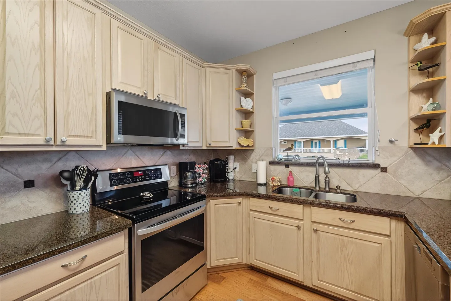 Kitchen corner featuring light wood cabinetry, dark speckled countertops, a stainless steel microwave, and an electric stove.