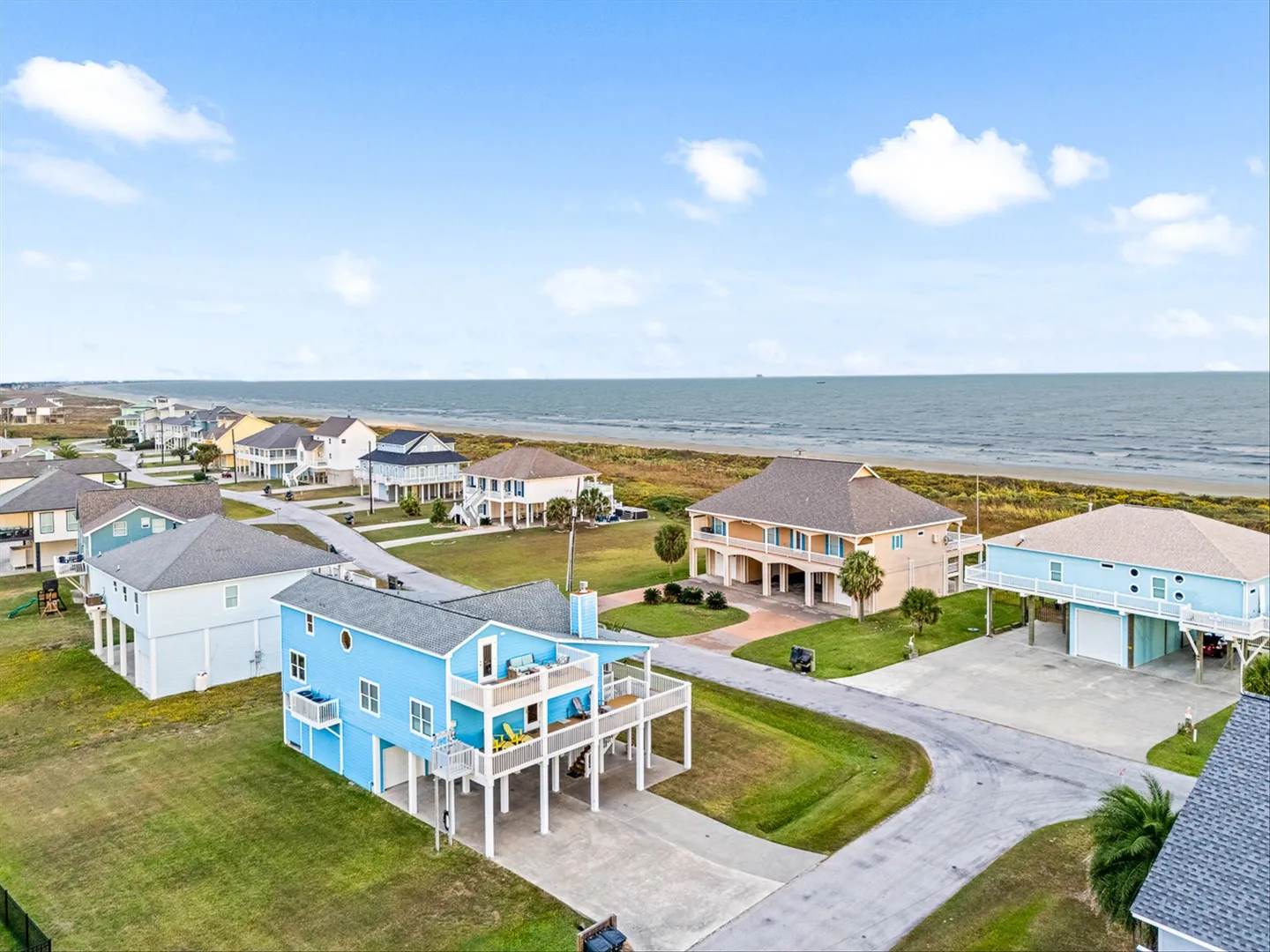 Aerial view of a coastal neighborhood with stilted beach houses along a road near the ocean.