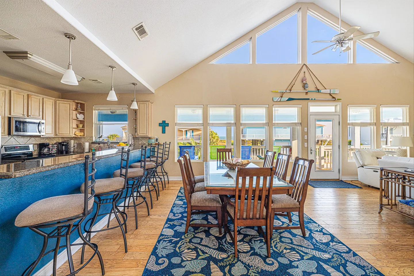 Open-concept dining area and kitchen with vaulted ceilings, large windows, and a blue breakfast bar.