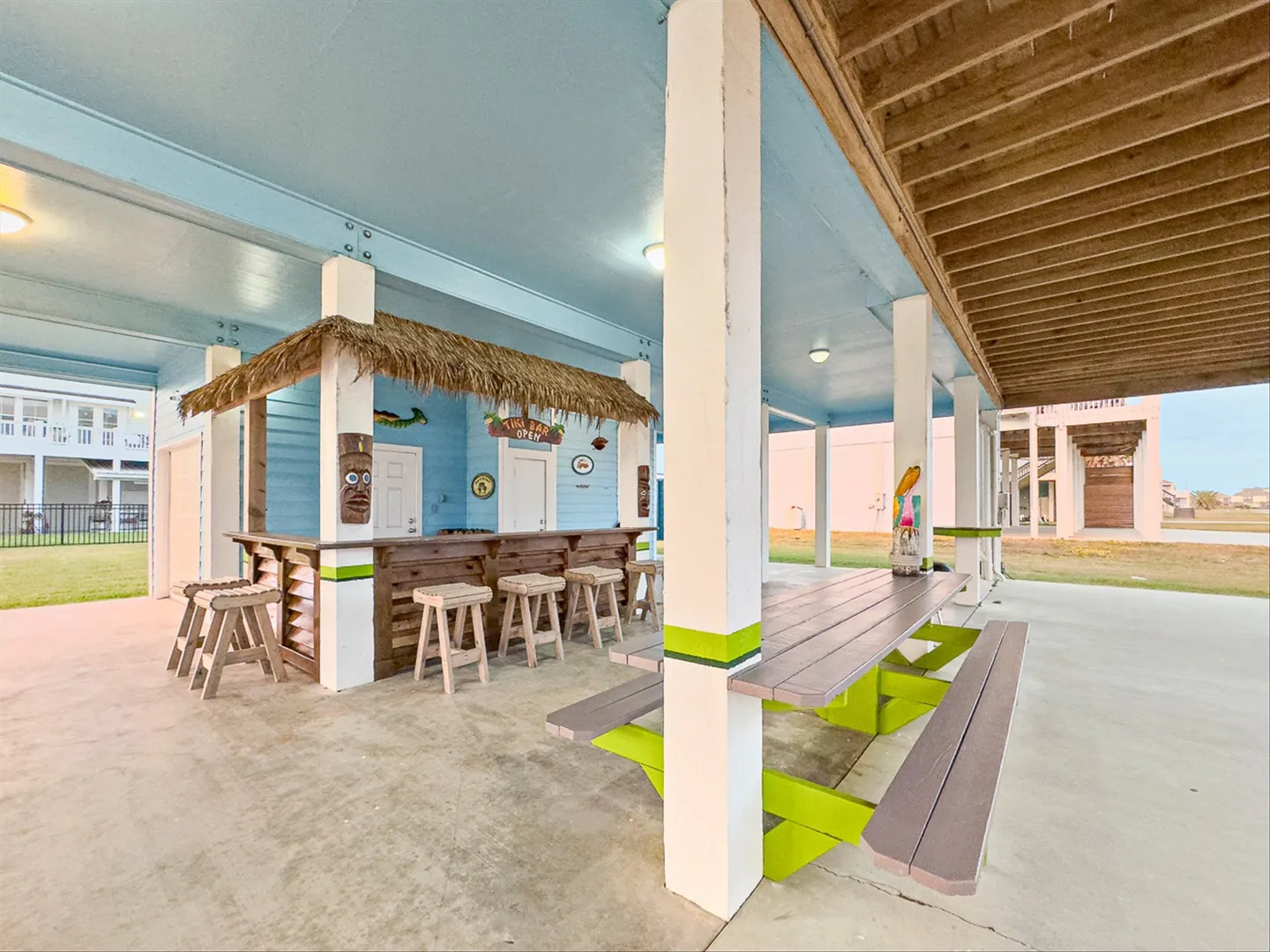 Covered outdoor patio area featuring a thatched-roof tiki bar with barstools and a nearby picnic table.