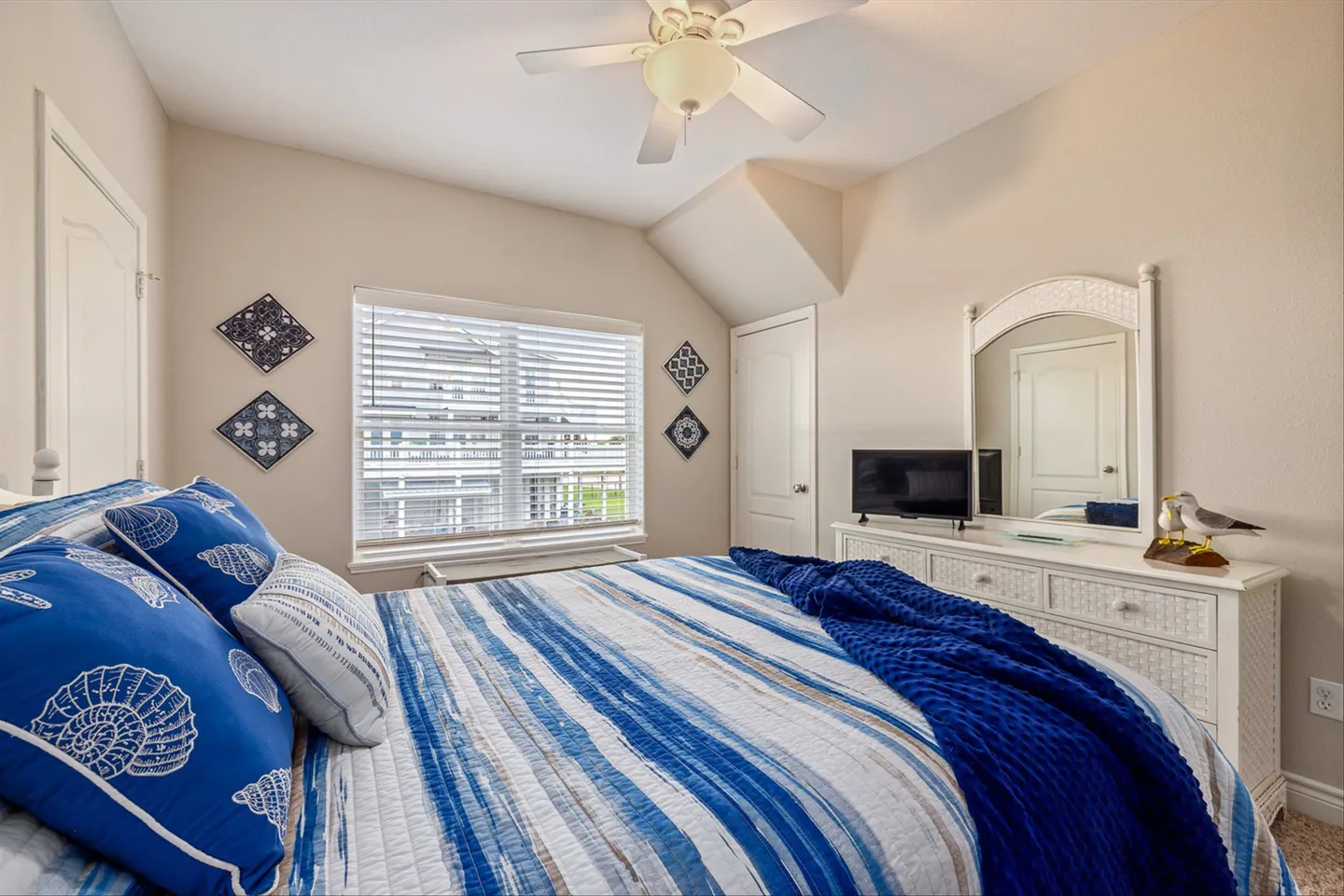 Bedroom featuring a bed with blue and white coastal bedding, a white dresser with mirror, and a window with blinds.