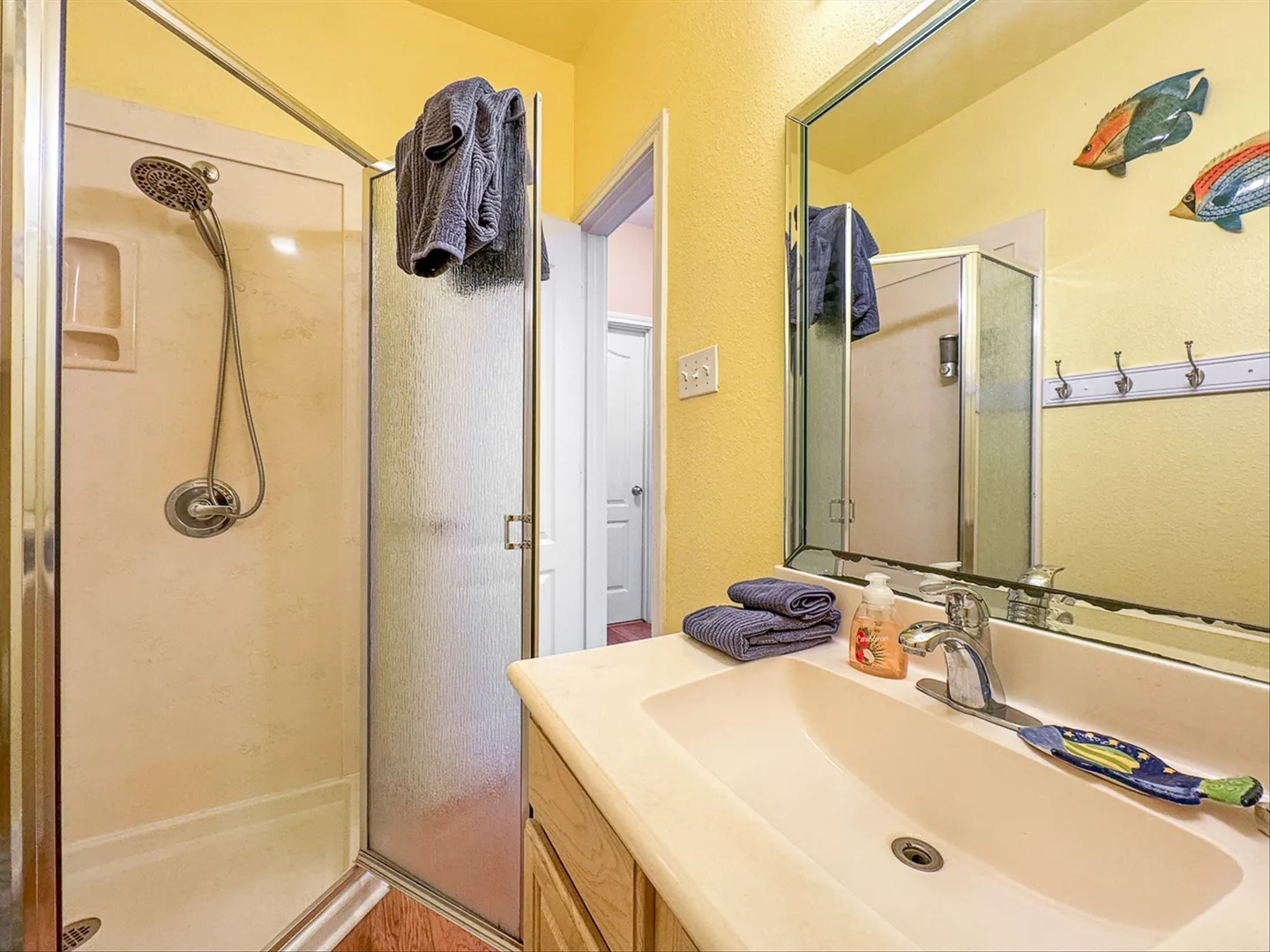 Bathroom with a vanity sink, mirror, and glass-door walk-in shower stall with yellow walls.