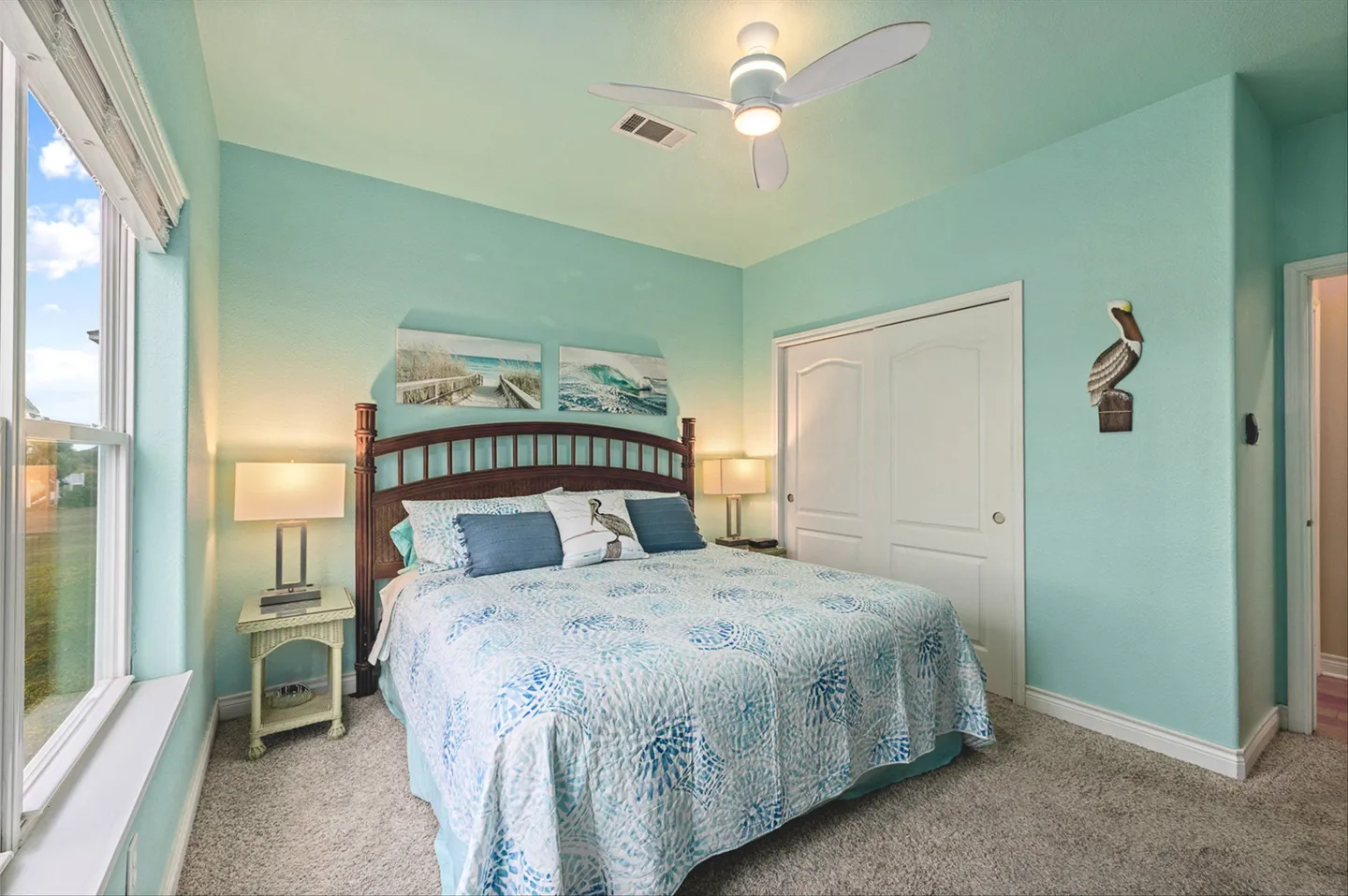 Bedroom with aqua walls, carpeted floor, large window, wooden headboard, and a ceiling fan.